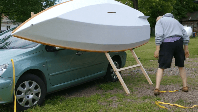 A man loading a boat onto a roof by use of a ladder