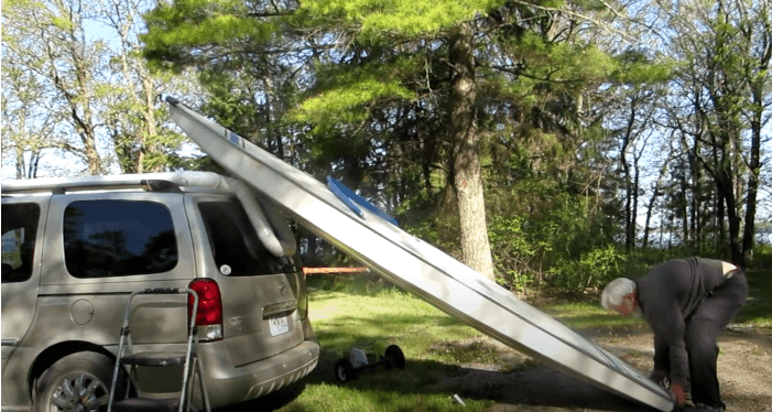 A man single-handedly sliding a boat onto a roof rack.