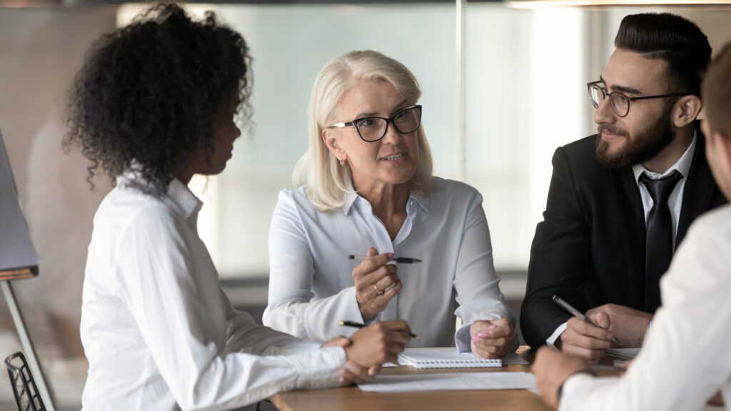 Motivated diverse businesspeople brainstorm discuss business ideas at company team meeting in office, multiracial colleagues cooperating at briefing consider paperwork engaged in negotiation together